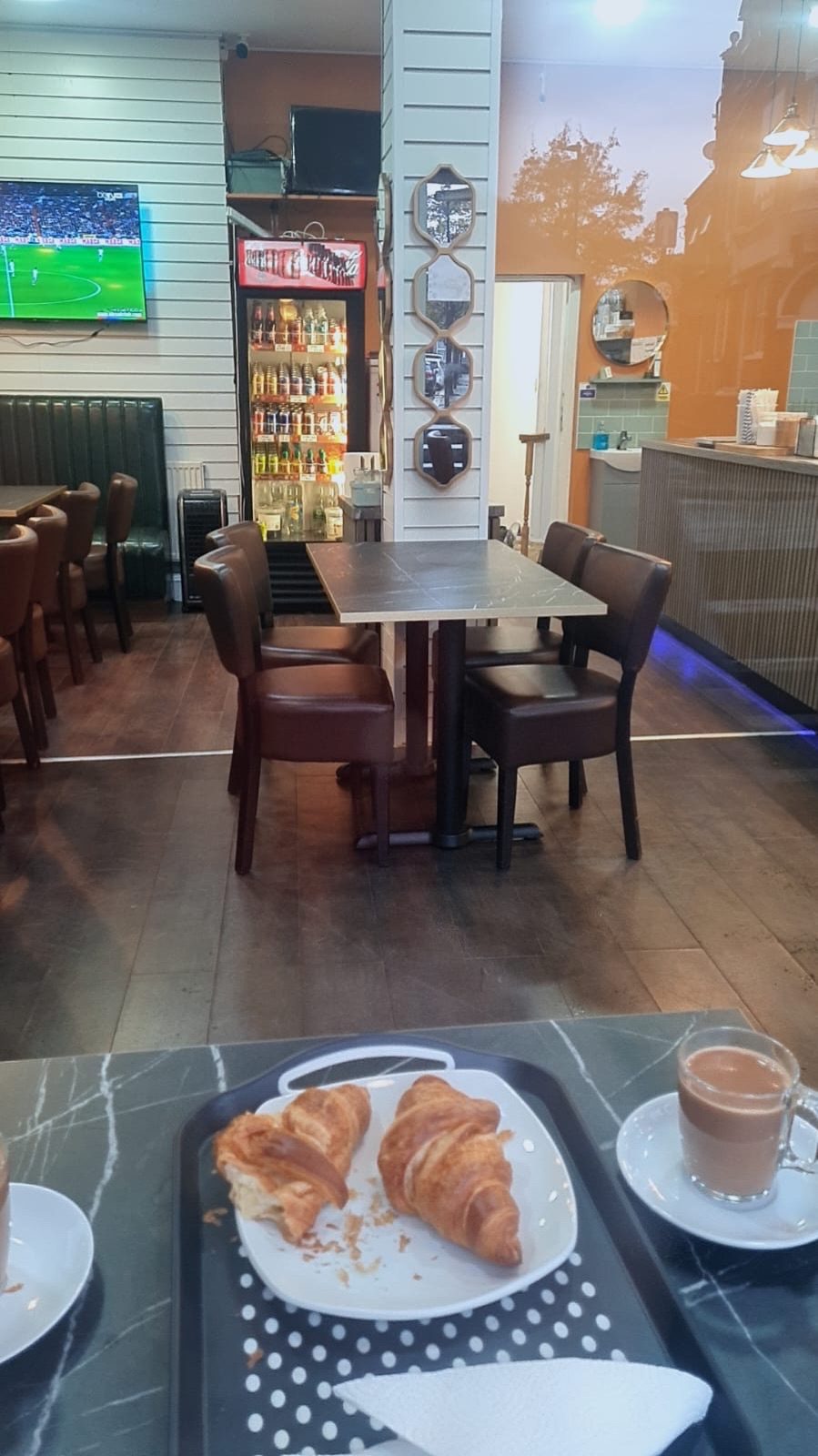 Inside the cafe past a tray with a croissant and coffee, wooden tables and brown leather chairs